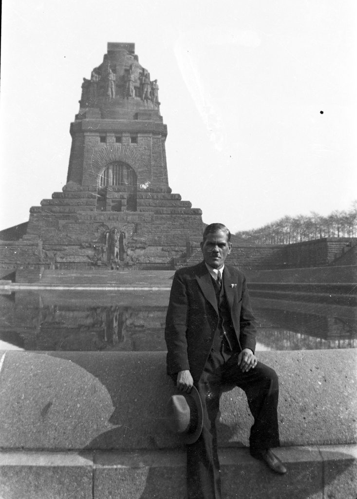 A black and white photograph showing Sakhawat Hussein Khan posing in front of the Völkerschlachtdenkmal in Leipzig.