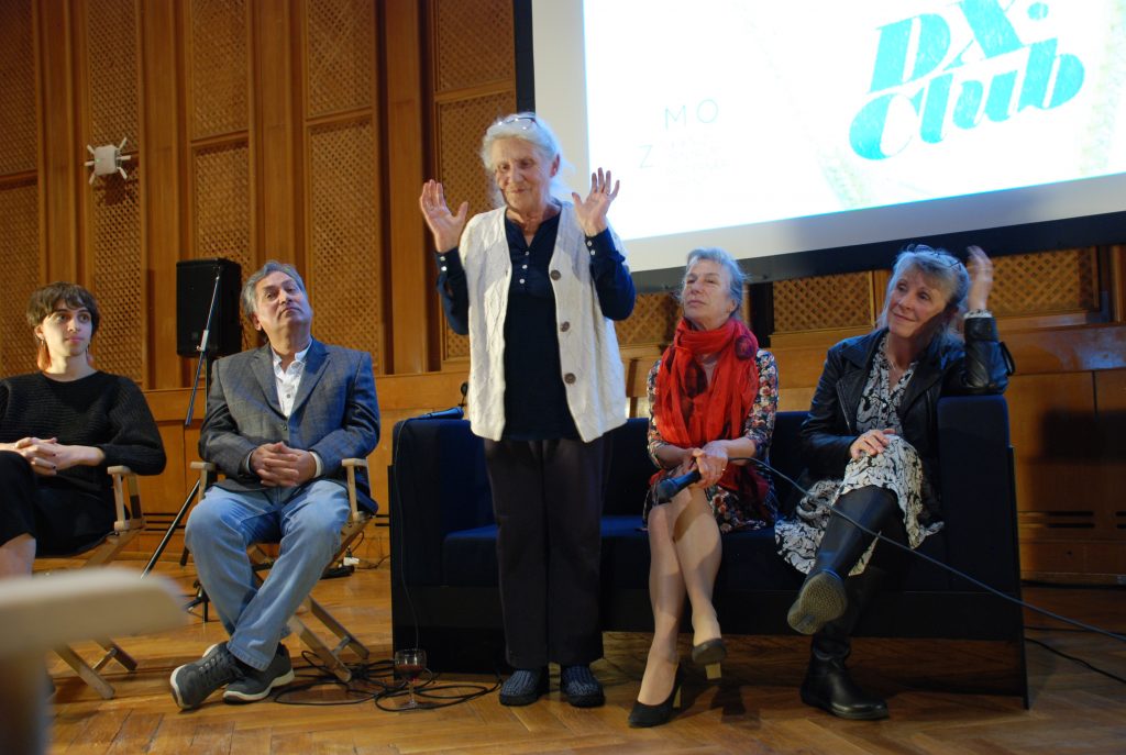 A former employee of RBI is standing up, telling a story. She is surrounded by three other former employees as well as the editor of the film, all of them seated.