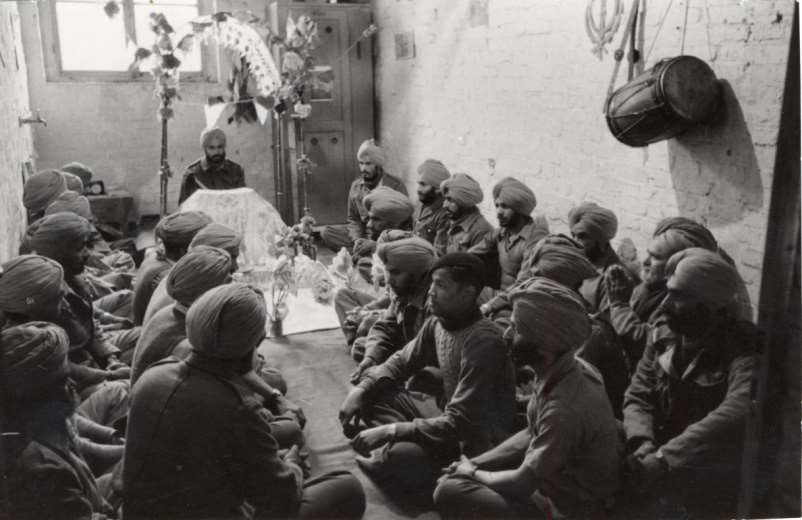 A group of about 25 Sikh POWs is sitting in a prayer room.