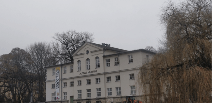 The picture shows the front of the Alpine Museum, with the entrance facing the Isarkanal. It is a cloudy winter’s day, and the surrounding trees are bare.